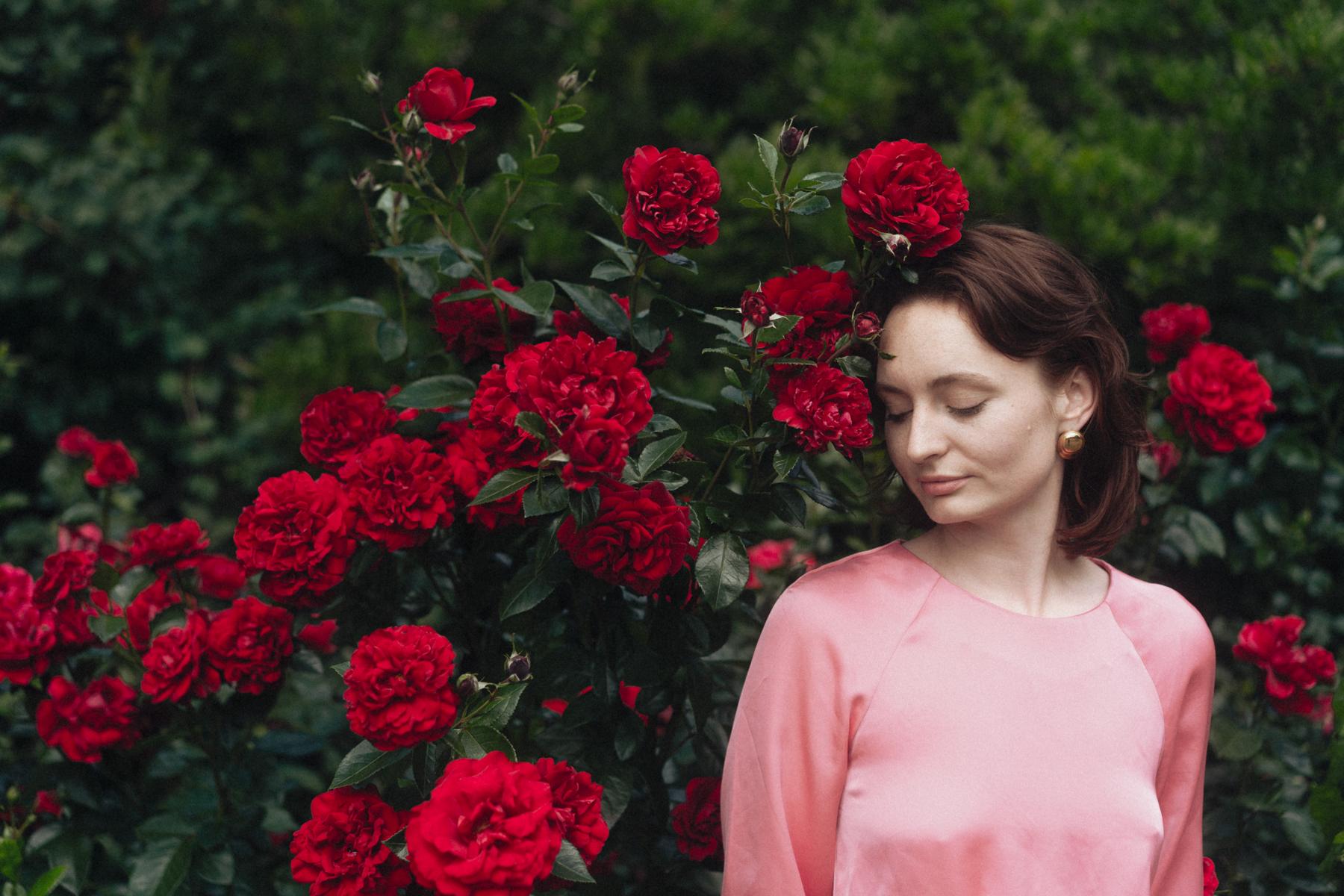 Daniela Taeger mit geschlossenen Augen vor einem blühenden roten Rosenstrauch